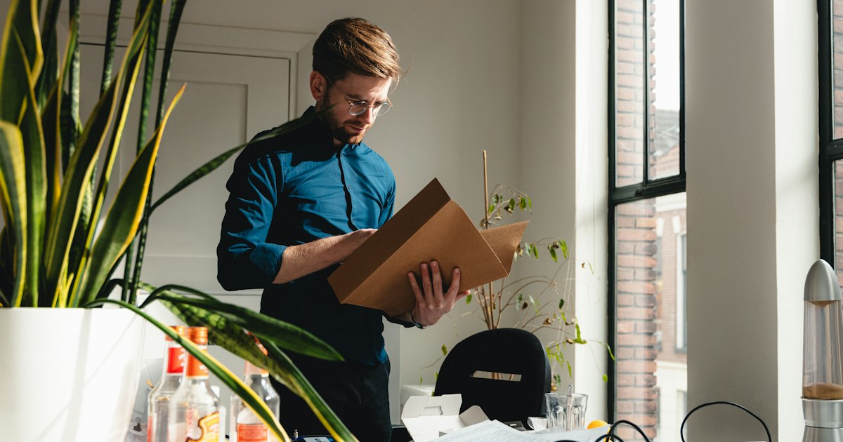 Responsabile e-commerce controlla un pacco e i dati di prodotto per preparare il negozio agli acquisti degli agenti AI